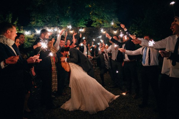 Bride and groom hug outside nighttime shot and guests dancing kissing couple