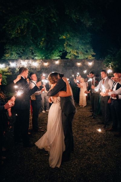 Bride and groom hug outside nighttime shot and guests