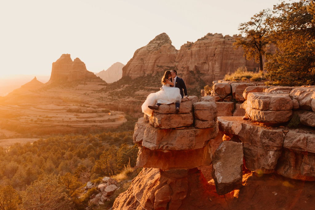 Couple take in the view as they sick on top of a rock on cliff kissing kiss