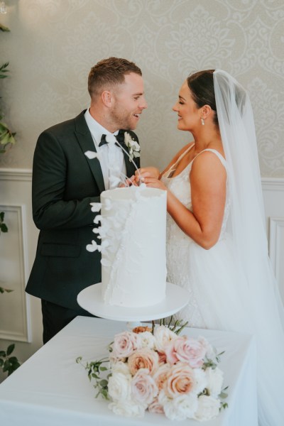 Bride and groom cut the white wedding cake covered in flowers