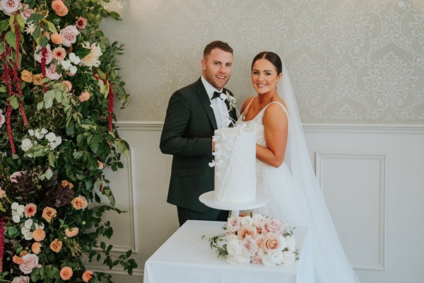 Bride and groom cut the white wedding cake covered in flowers