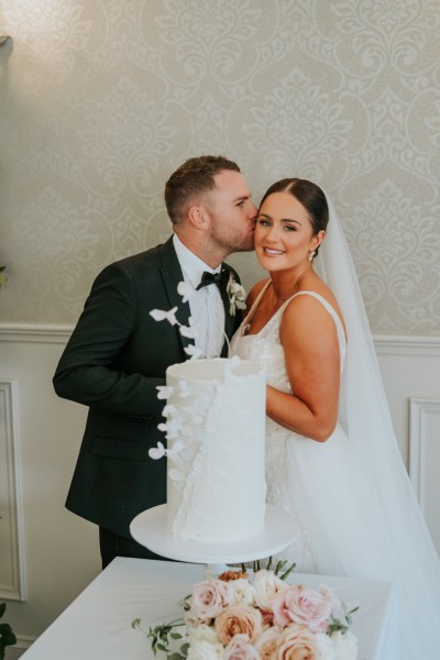 Bride and groom cut the white wedding cake covered in flowers