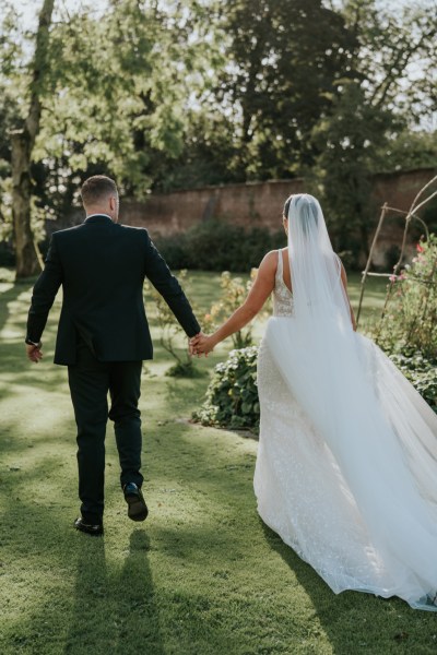 Bride and groom walk hand in hand in garden