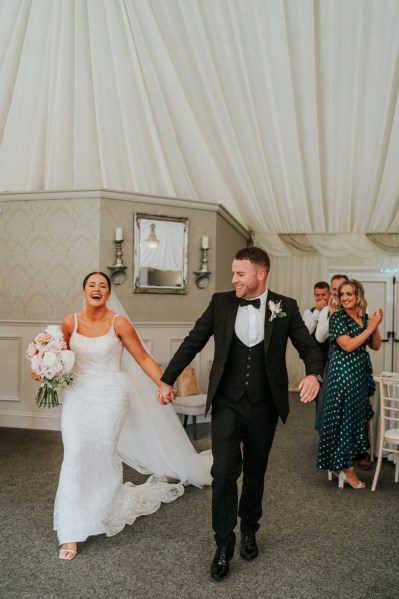 Bride and groom holding hands entering ballroom guests clap