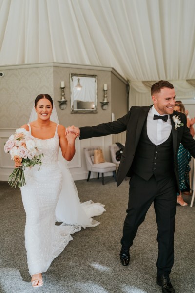 Bride and groom holding hands entering ballroom