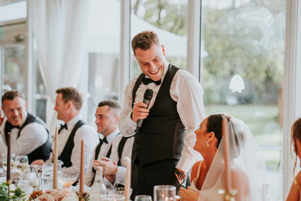 Groom during his speech bride laughing at table