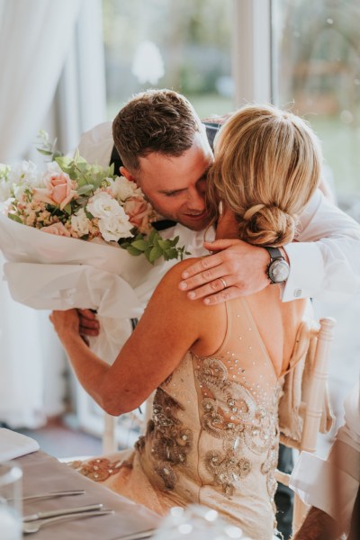 Groom hugs mother bouquet of flowers guest