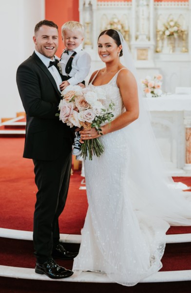 Bride groom and son smiling for the camera pink roses church interior