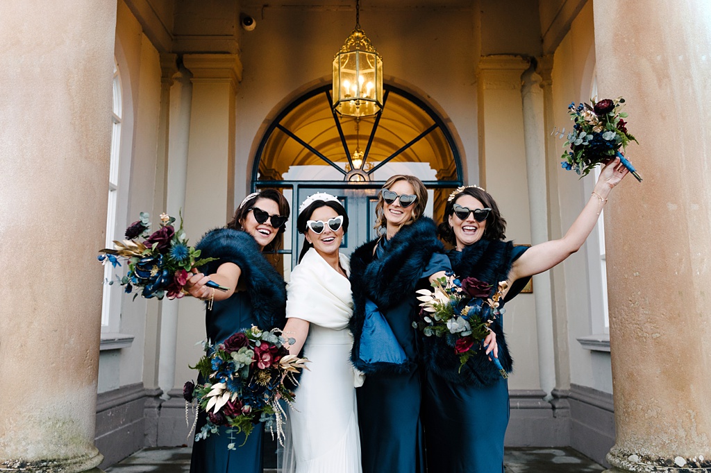 Bride and bridesmaids pose wearing sunglasses in front of door