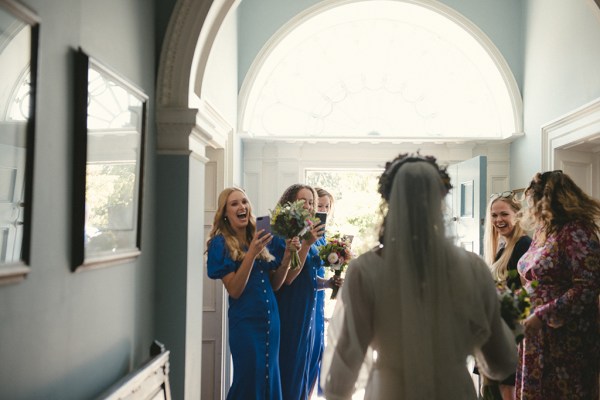 Bridesmaids in blue react to the bride wearing a veil