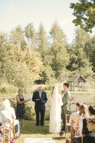 Bride and groom at alter to wedding ceremony with officiant and guests in background back of bridal gown/veil detail