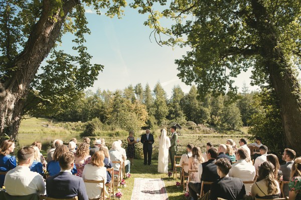 Bride and groom at alter to wedding ceremony with officiant and guests in background back of bridal gown/veil detail