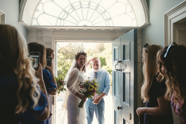 Bride and father smiling with bridesmaids in shot