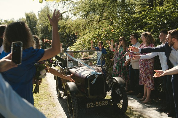 Bride and groom in wedding car smiling guests wave them off