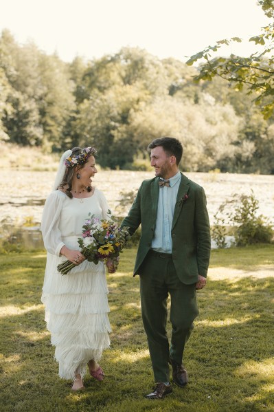 Bride holding bouquet of flowers laughing with groom arm in arm embracing