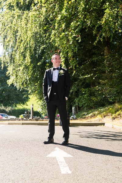 Groom stands in garden sun shining