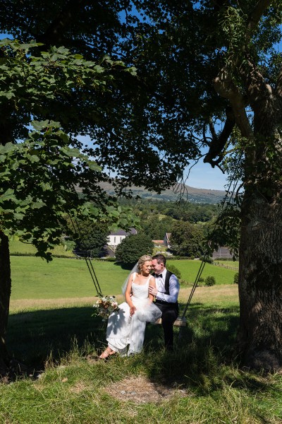 Bride and groom sit on swing together landscape background in background scenery sunshine forest trees setting