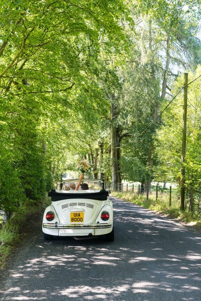 Couple bride and groom sitting in white wedding car in forest/park bouquet in the air