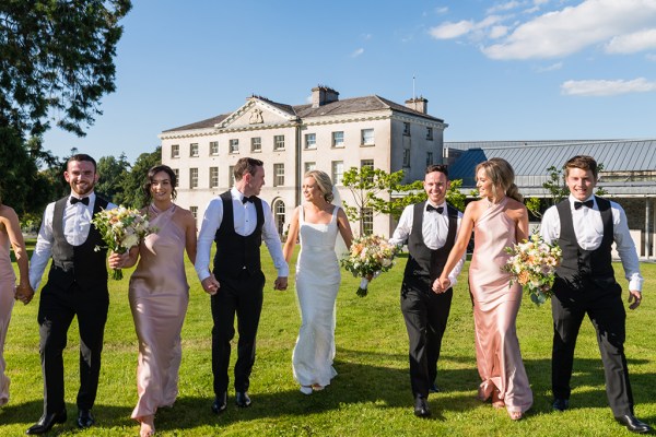 Exterior wedding venue bride groomsmen groom bridesmaids on grass holding hands