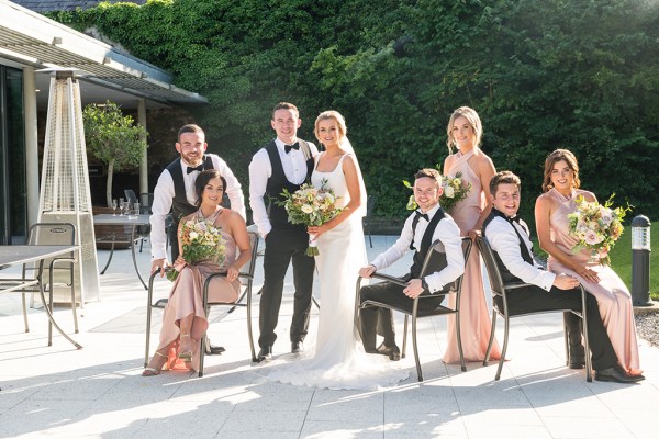 Bride groom bridesmaids groomsmen sitting on chairs in the sunshine