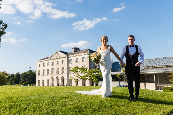 Bride and groom on grass exterior wedding venue hand in hand