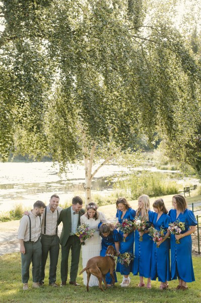 Bride groom bridesmaids and groomsmen best man pose for a picture on the grass in park lake in background