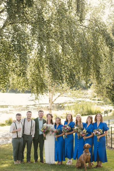 Bride groom bridesmaids and groomsmen best man pose for a picture on the grass in park lake in background