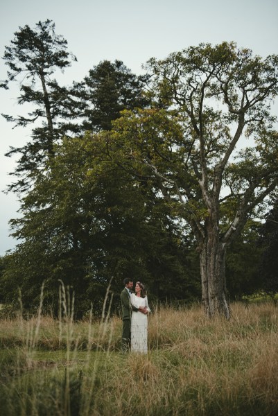 Bride and groom in park onlooking lake embracing looking at each other