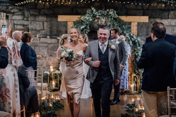 Bride holds bouquet in the air with groom and guests clapping exiting