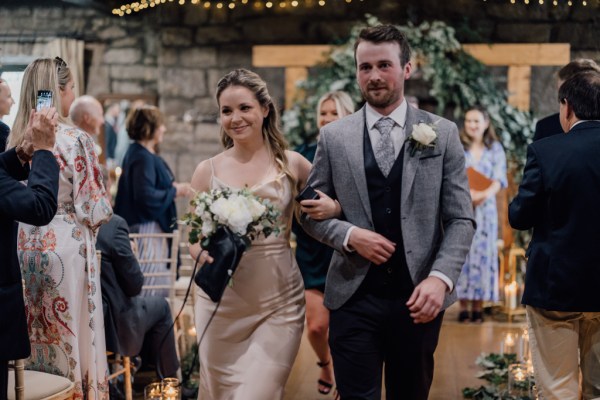 Bride holds bouquet in the air with groom and guests clapping exiting