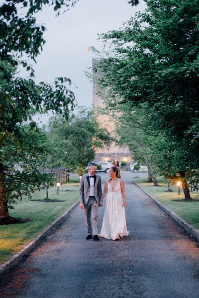 Bride and groom walk hand in hand in forest garden pathway setting