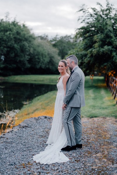 Bride and groom standing on ground beside fence in forest