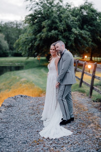 Bride and groom standing on ground beside fence in forest