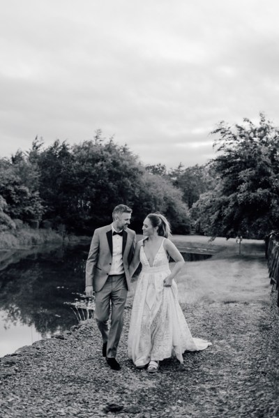 Black and white image of couple lake in background walking on grass