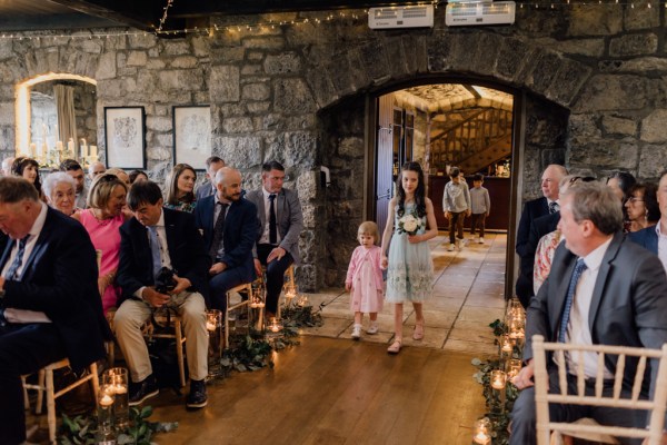 Two little girls walk down the aisle surrounded by guests