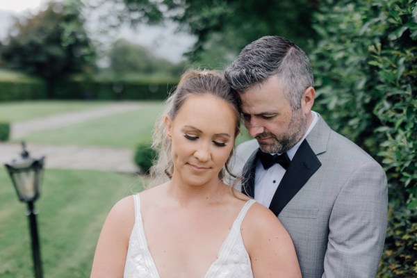 Bride and groom pose outside on the pathway holding bouquet of flowers