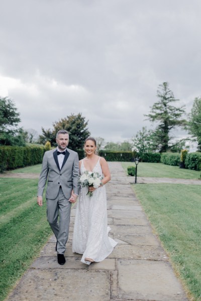 Bride and groom walk outside on the pathway holding bouquet of flowers