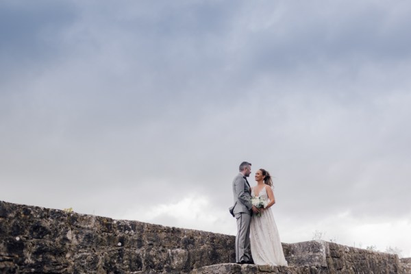 Bride and groom stand on rocks looking at each other