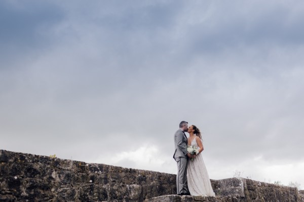 Bride and groom stand on rocks and kiss/kissing wide shot