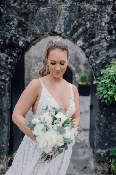 Bride looks down at bouquet in front of archway