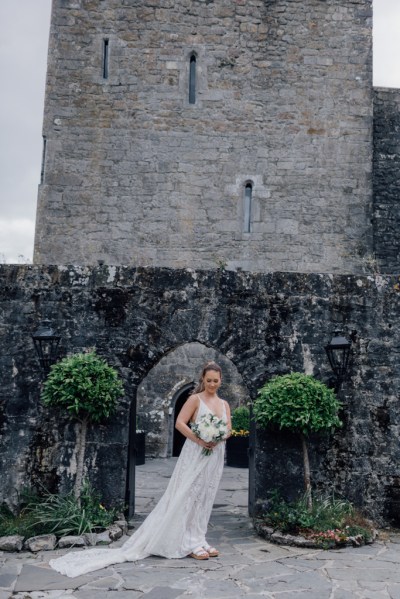 Bride on her own in garden posing under archway holding bouquet