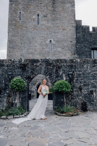 Bride on her own in garden posing under archway holding bouquet