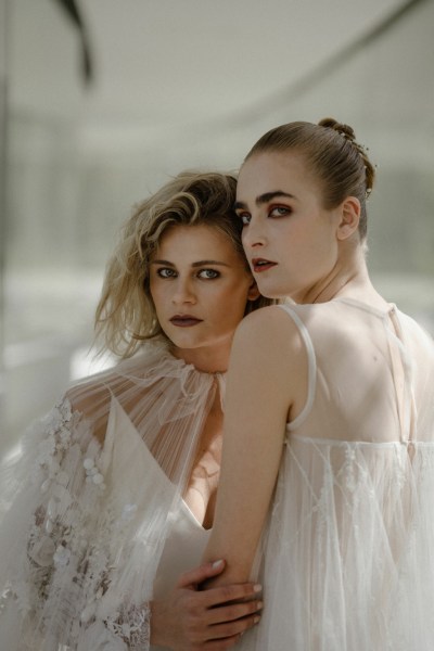 Mid close up of two brides pose for camera wearing white bridal gowns/dresses