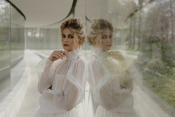 blonde curly haired woman wavy sitting against window relfection ruffle neckline bridal gown detail