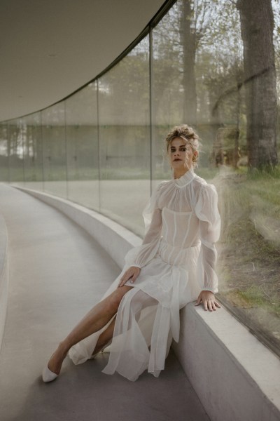 blonde curly haired woman ruffle neckline detail bridal gown/dress sitting on ledge