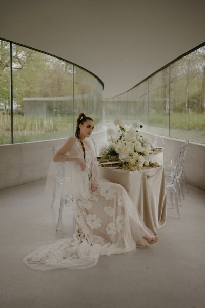 Bride sits and poses surrounded by white roses and flowers floral train dress bridal gown lace detail