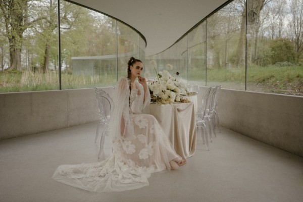 Bride sits and poses surrounded by white roses and flowers floral train dress bridal gown lace detail