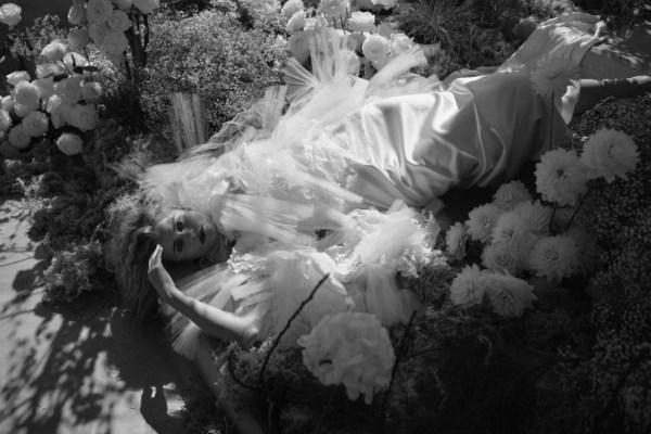 Black and white image of blonde woman lying in bed of flowers silky dress bridal gown white roses