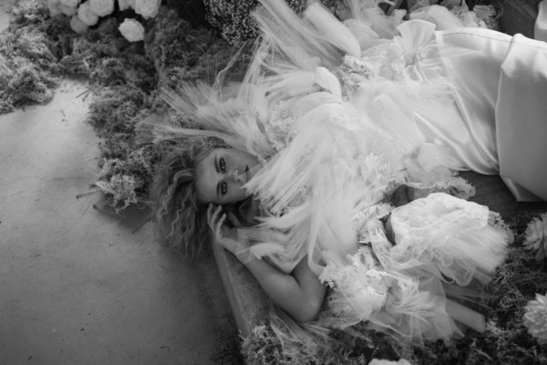 Black and white image of blonde woman lying in bed of flowers silky dress bridal gown white roses