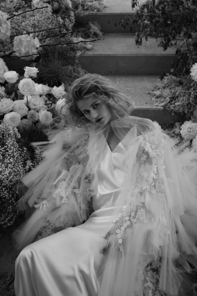 Black and white image of blonde woman lying in bed of flowers silky dress bridal gown white roses